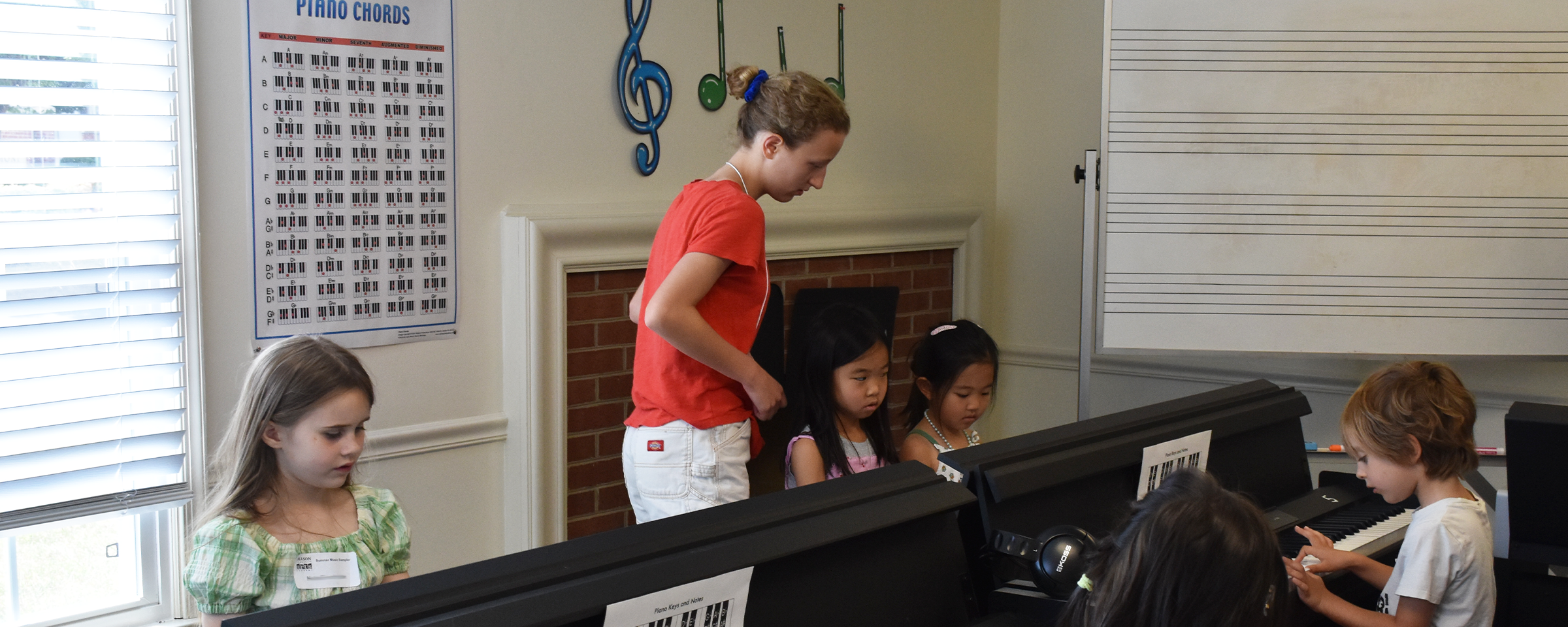An intern assisting children with playing the piano